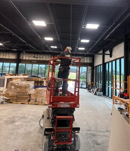 Commercial electrician on a red scissor lift installing high-bay warehouse lighting and commercial wiring