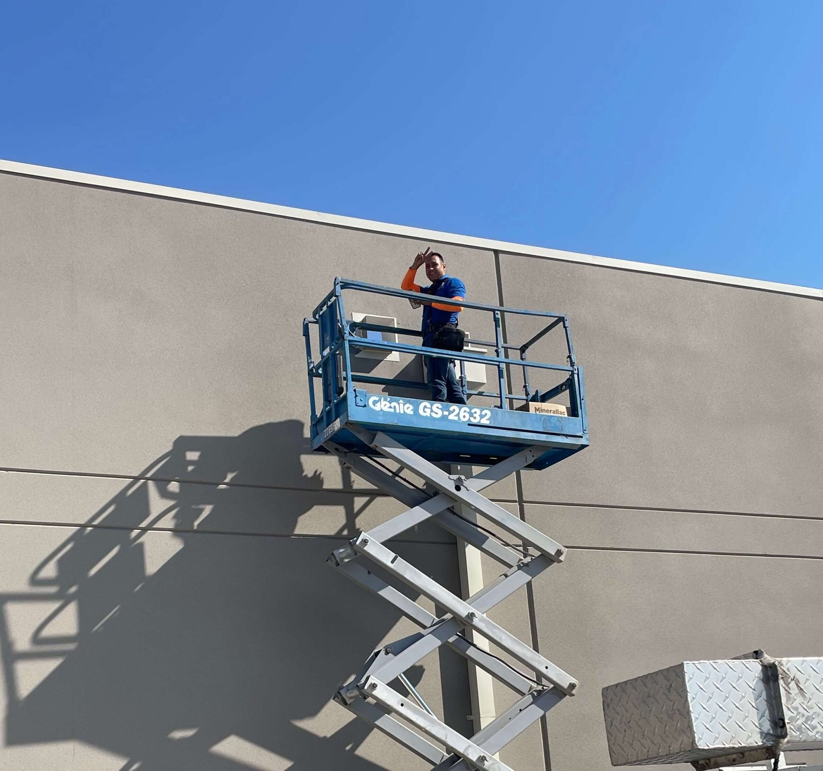 Industrial electrician using a blue scissor lift for exterior high-voltage power installation on a commercial building